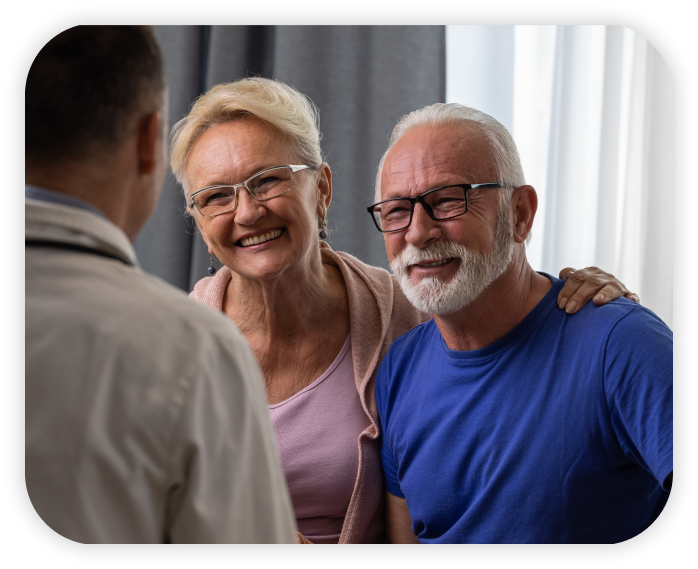 Doctor conversing with patient and family member. Doctor's back facing the camera while patients with happy demeanors engage in conversation.