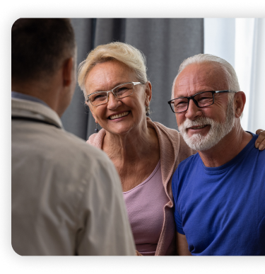 Doctor conversing with patient and family member. Doctor's back facing the camera while patients with happy demeanors engage in conversation.